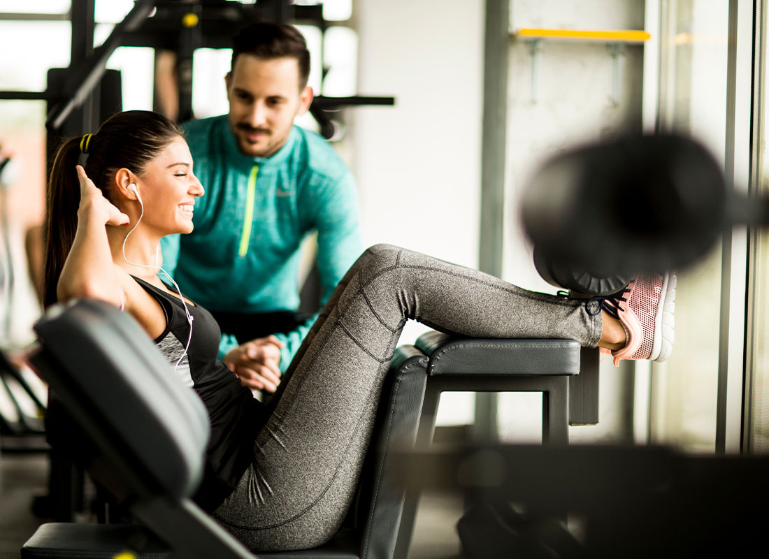 Personal Trainer Insurance - Smiling Woman Exercising in the Gym With the Help of Her Personal Trainer While Listening to Music