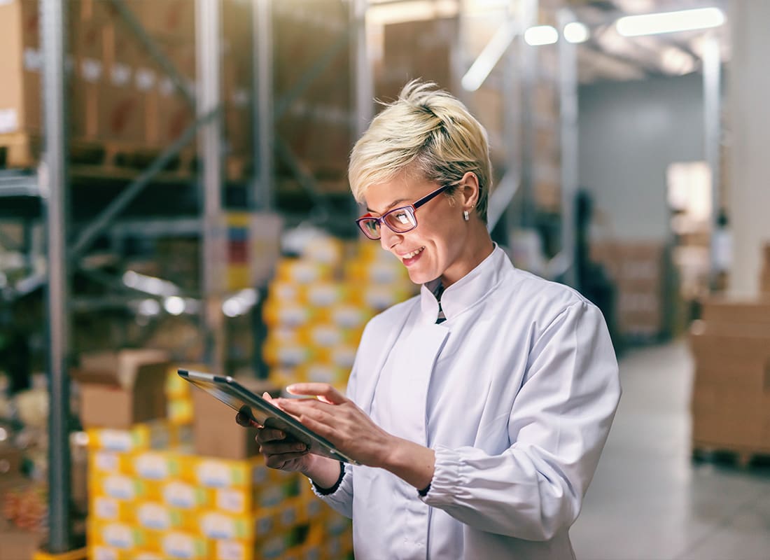 About Our Agency - Young Blonde Woman in a White Uniform Using a Tablet in a Warehouse