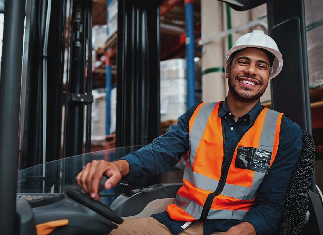 Insurance Solutions - Young Forklift Driver Sitting in a Vehicle at a Warehouse Smiling and Looking at Camera
